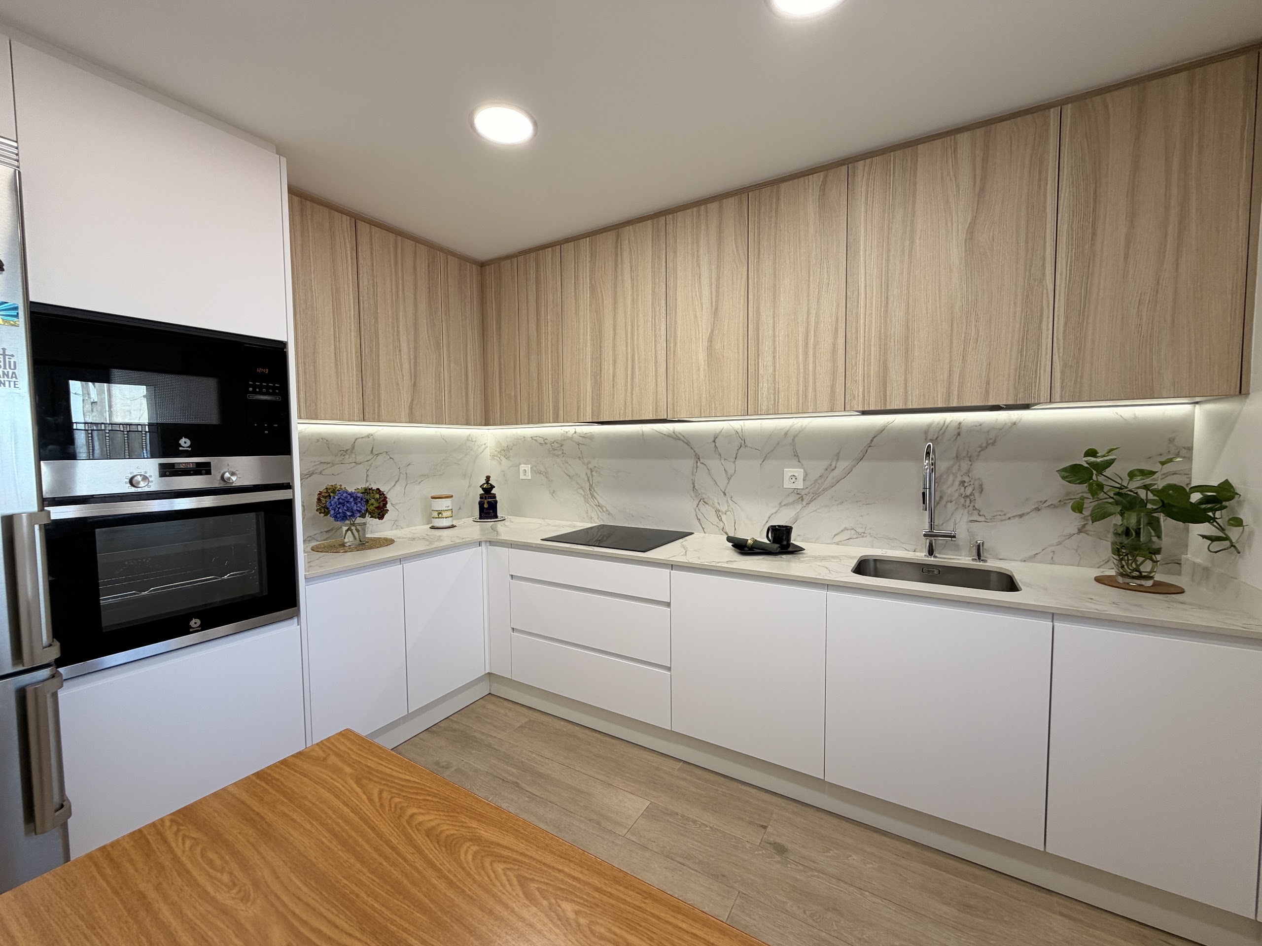 Cocina en L blanca y madera Oak Biscuit con luz led bajo los muebles altos